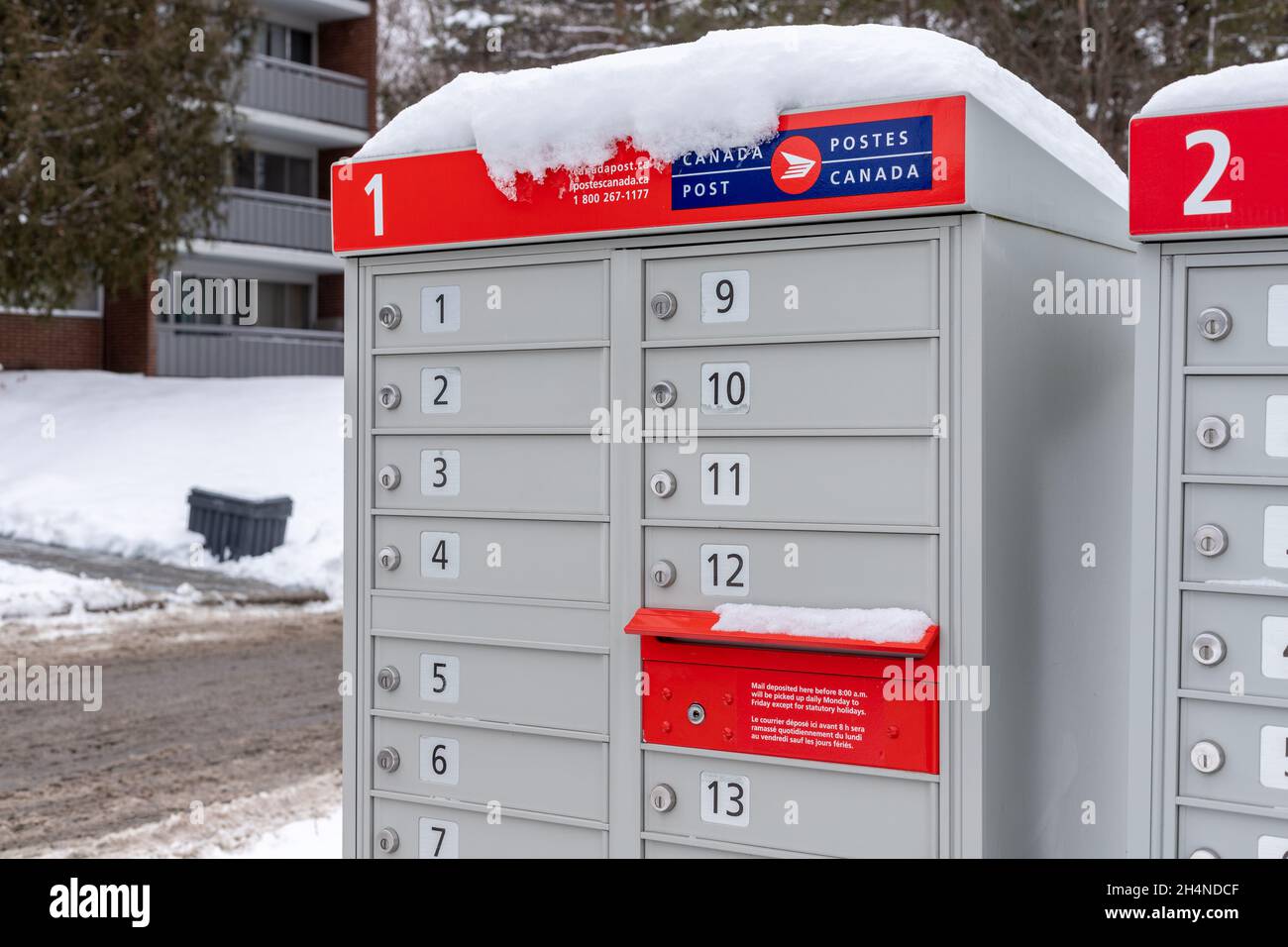 Boîtes aux lettres de postes Canada avec enseigne rouge en français et en anglais près de la maison en hiver Banque D'Images