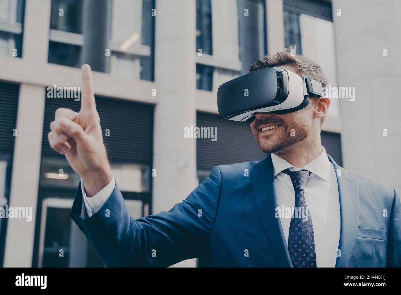Homme d'affaires barbu souriant avec barbe de 3 jours portant des lunettes VR, regardant quelque chose dans la réalité virtuelle Banque D'Images