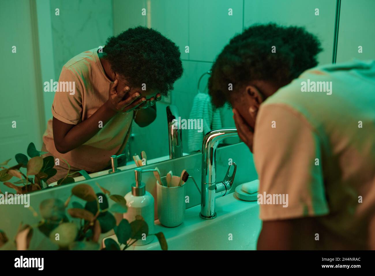 Une jeune femme africaine lavant son visage avec de l'eau avant de dormir debout dans la salle de bains en face du miroir Banque D'Images