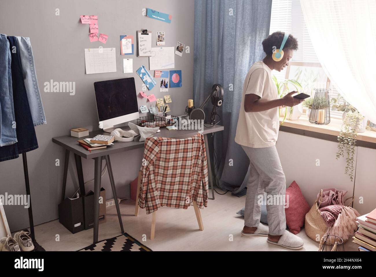Jeune femme africaine dans un casque sans fil utilisant son téléphone portable pour écouter de la musique dans la pièce Banque D'Images