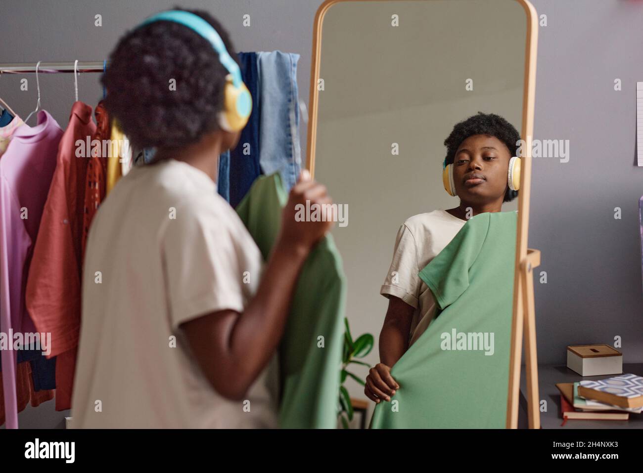 Femme africaine en casque sans fil essayant la nouvelle robe en se tenant devant le miroir dans la pièce Banque D'Images