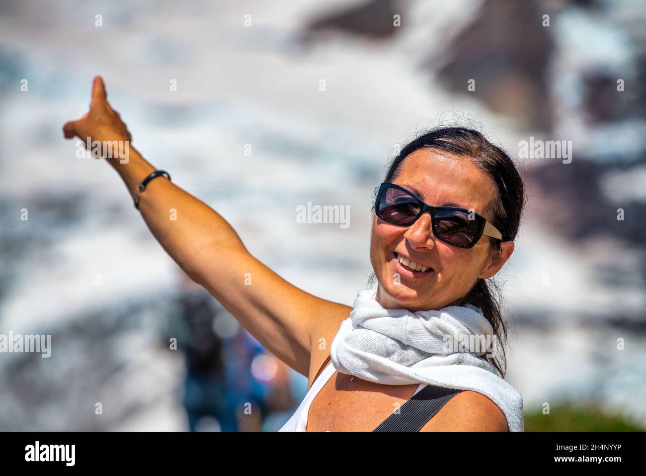 Une femme souriante se coince le doigt dans une belle montagne enneigée en été Banque D'Images