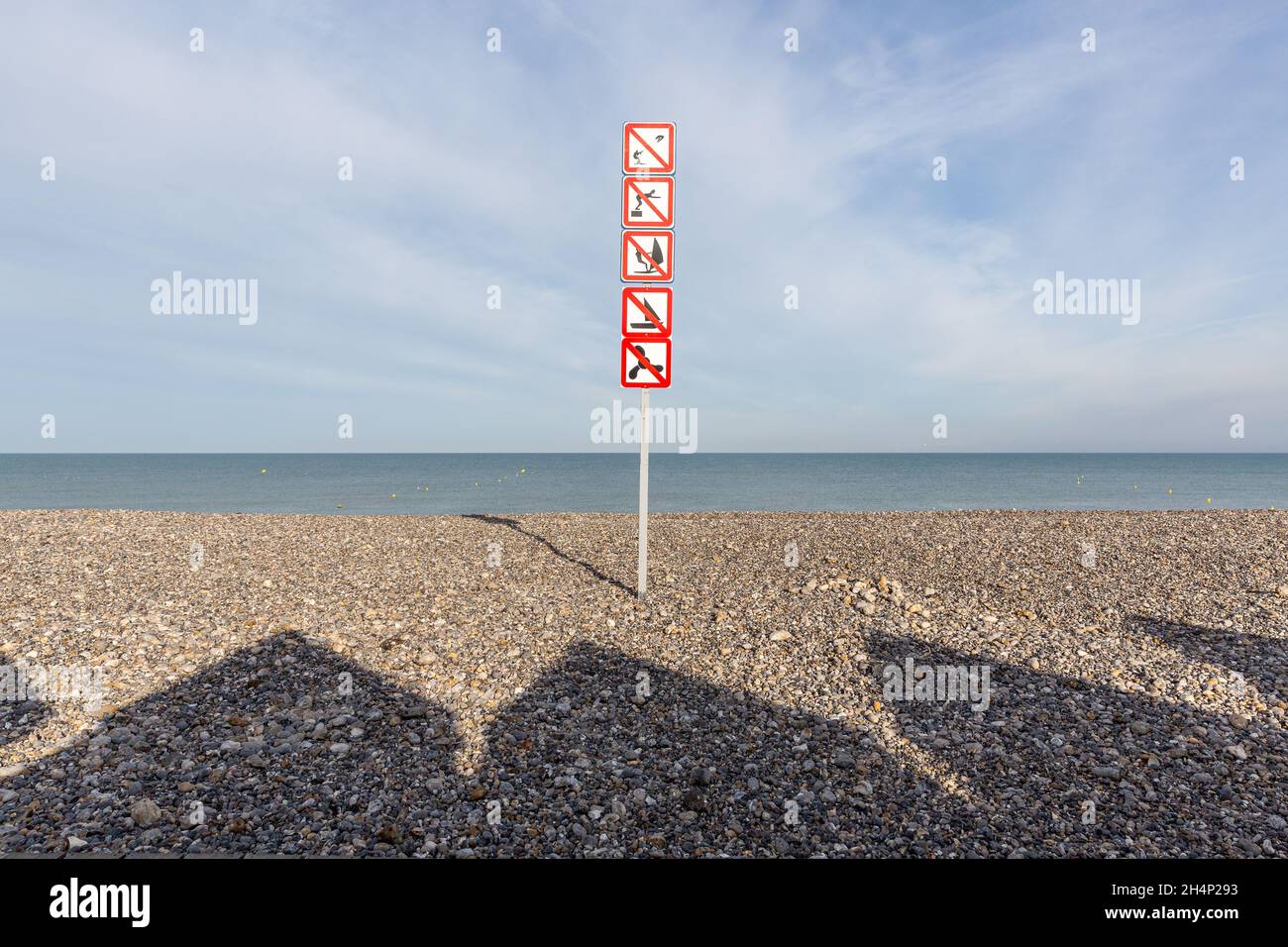 Ombres des huttes de plage projetant sur les galets de la plage de Cayeux-sur-Mer.Divers panneaux d'interdiction.Opal Coast, France Banque D'Images