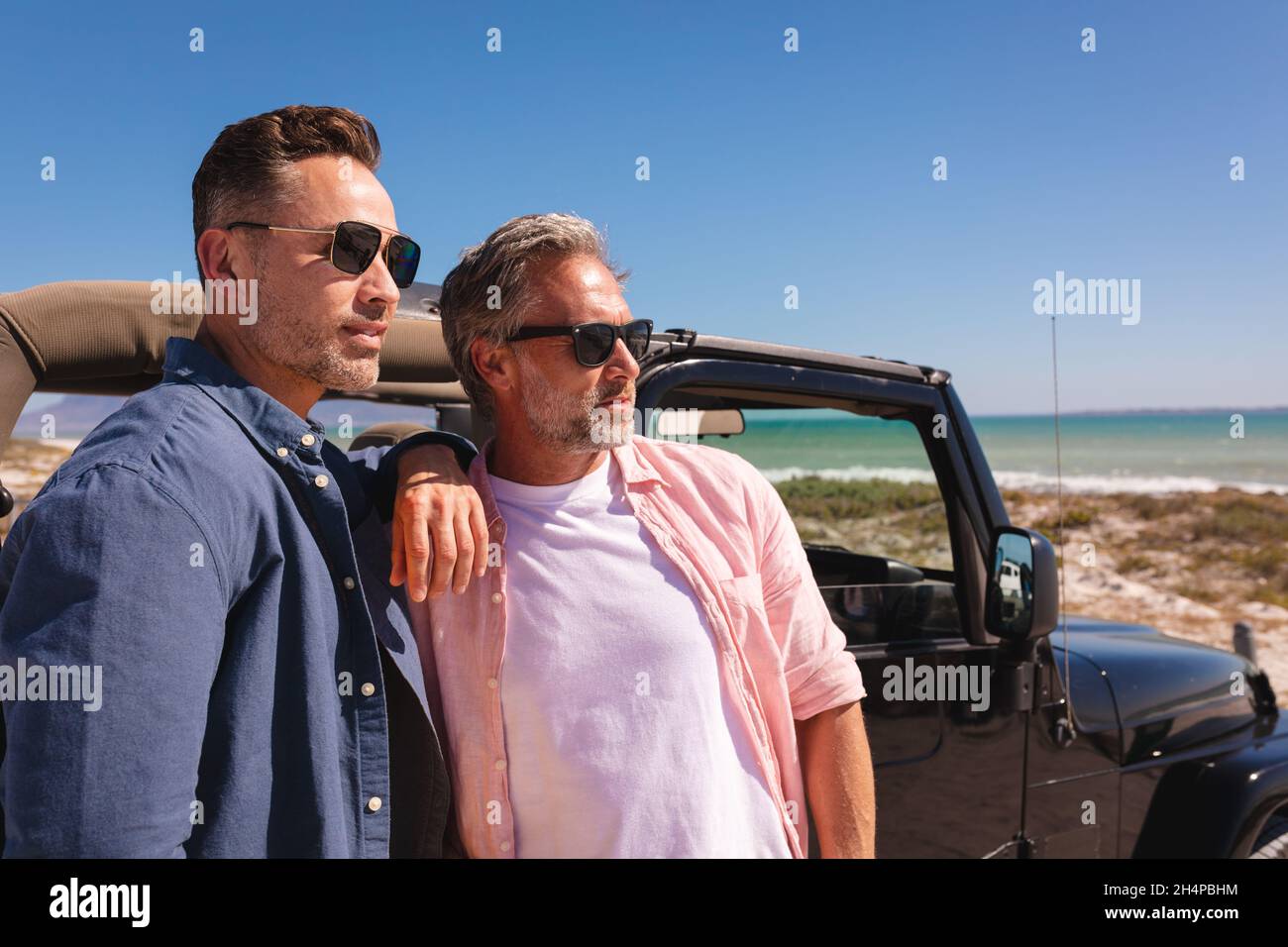 Un heureux couple de hommes gais de race blanche embrassant par une voiture au bord de la mer Banque D'Images