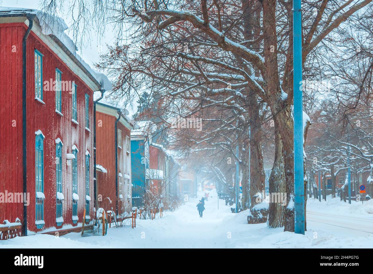 Tempête de neige en hiver.Les gens marchent dans une rue enneigée avec des maisons anciennes et colorées.Route enneigée avec bâtiments rouges.Chute de neige en ville.Architecture finlandaise. Banque D'Images