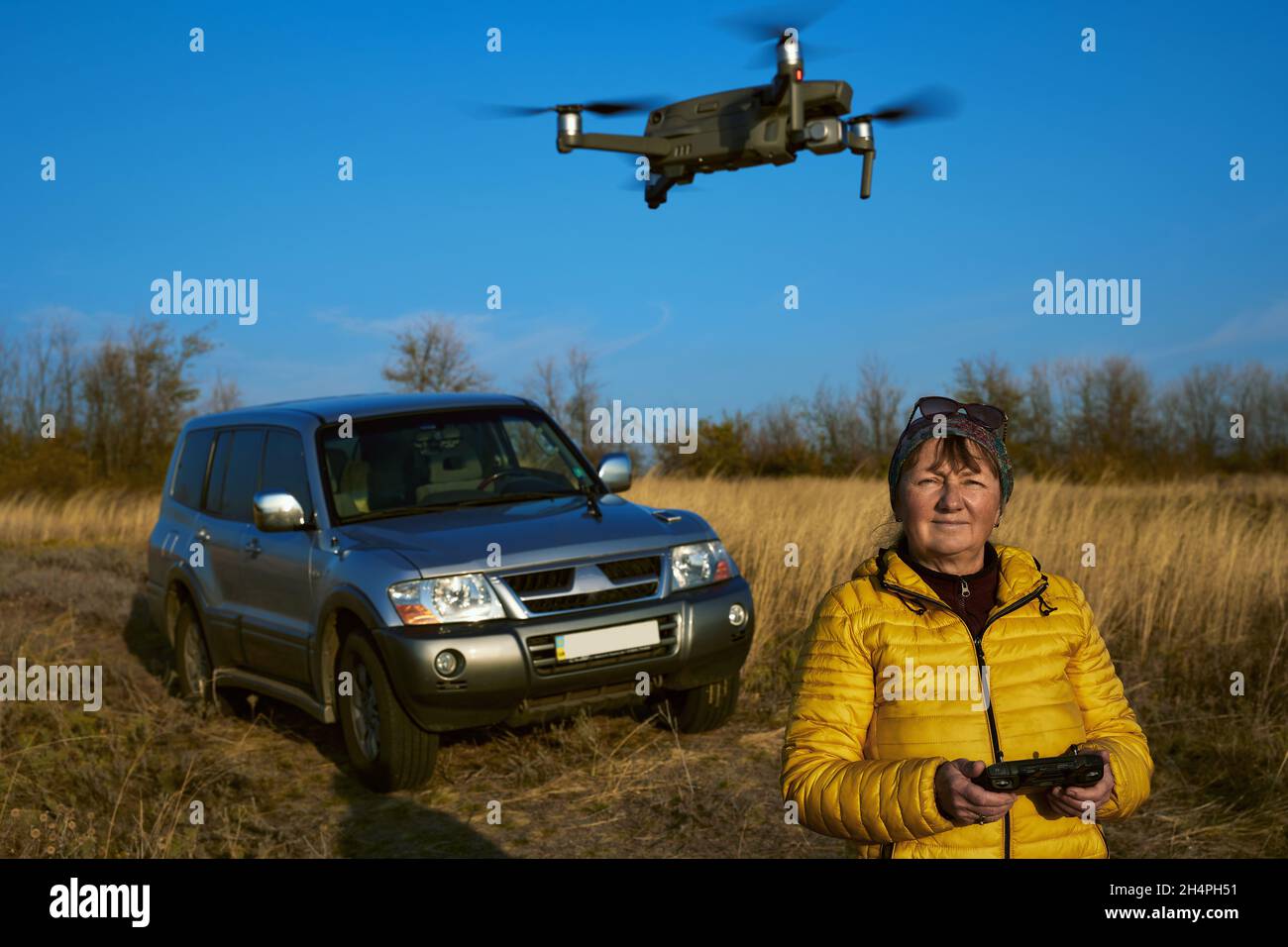 Belle femme adulte mature pilote drone sur voiture tout-terrain et herbe d'automne Banque D'Images