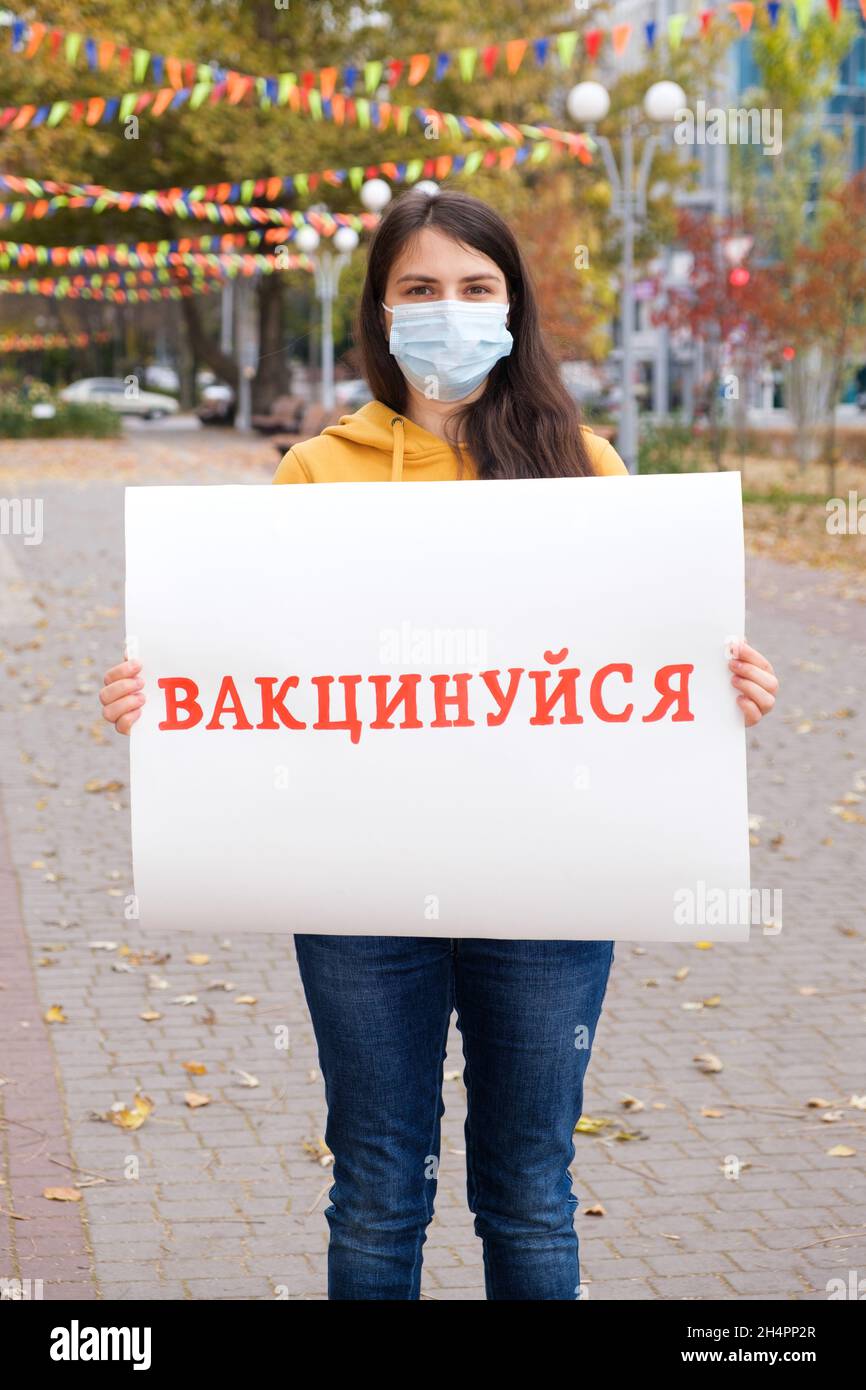 Une femme dans un masque médical tient une affiche avec une inscription, traduite de l'ukrainien se faire vacciner Banque D'Images