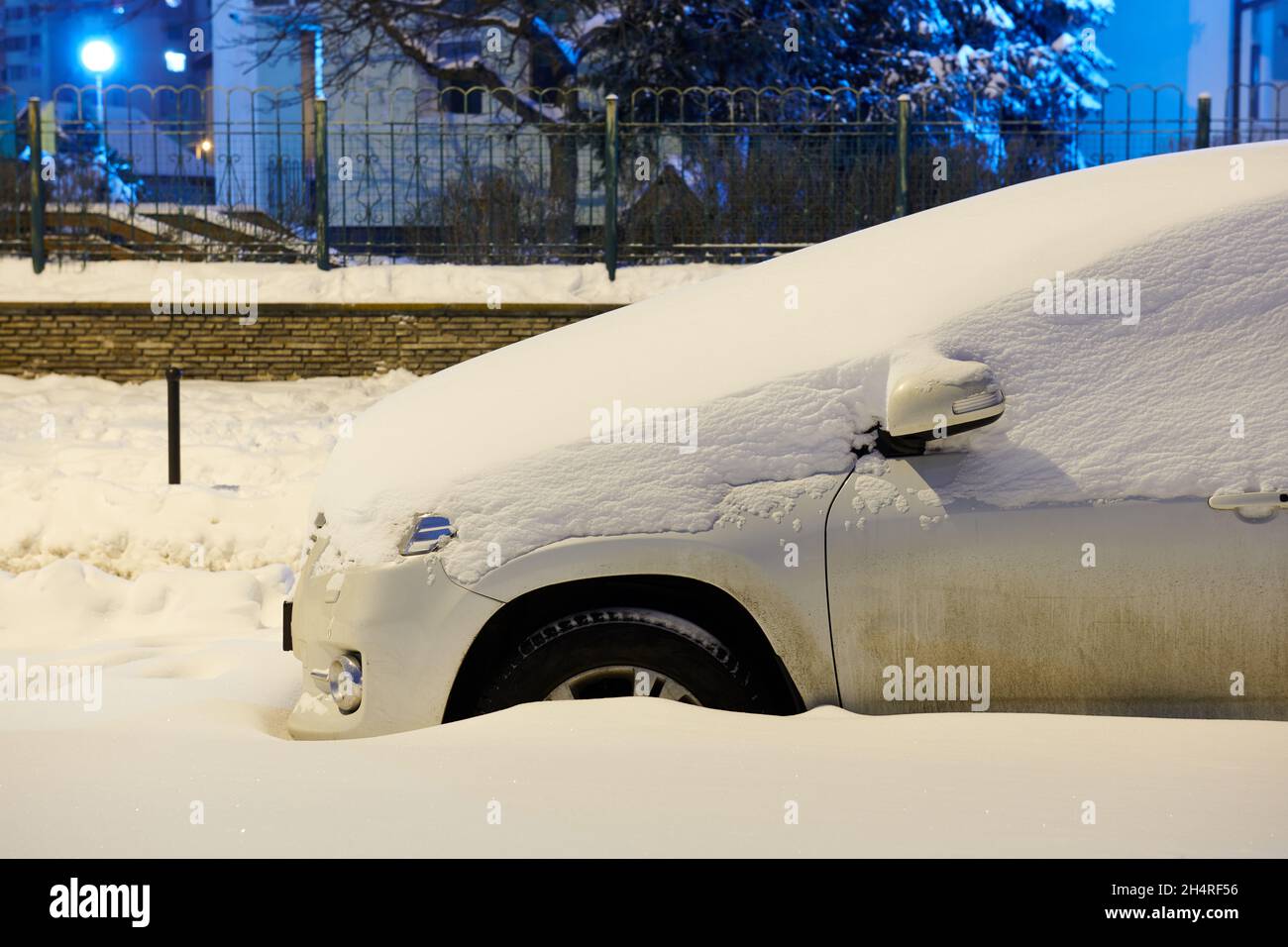 Voiture blanche recouverte de neige la nuit.Voiture garée dans la cour.Ville après la tempête de neige.Vue latérale.Gros plan. Banque D'Images