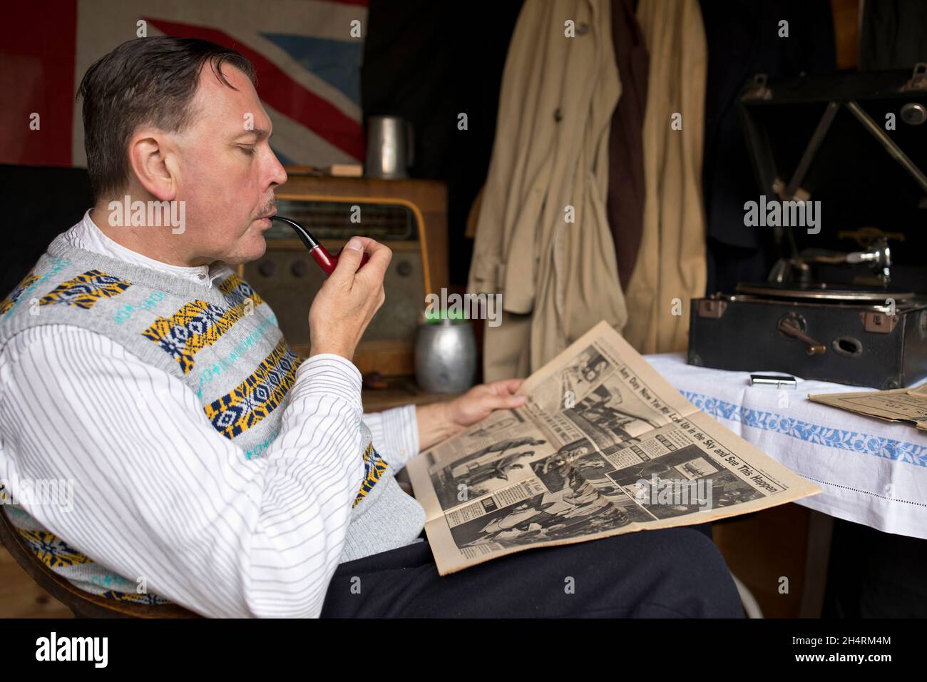 Royaume-Uni des années 1940 : l'homme fume la pipe, lisant le journal tout en listentant au disque gramophone. Banque D'Images