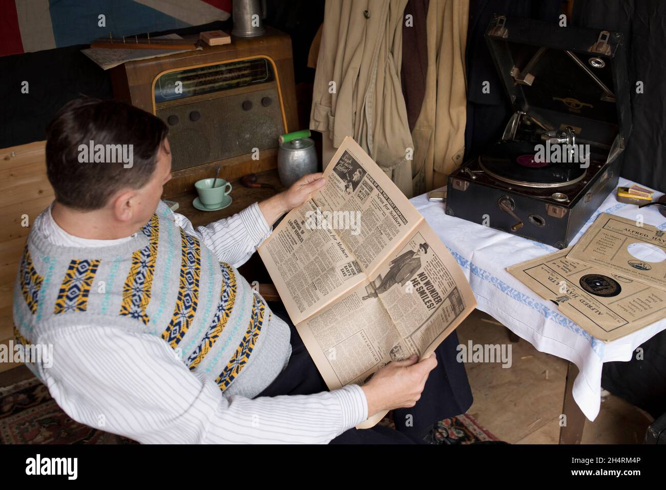 Royaume-Uni des années 1940 : l'homme fume la pipe, lisant le journal tout en listentant au disque gramophone. Banque D'Images