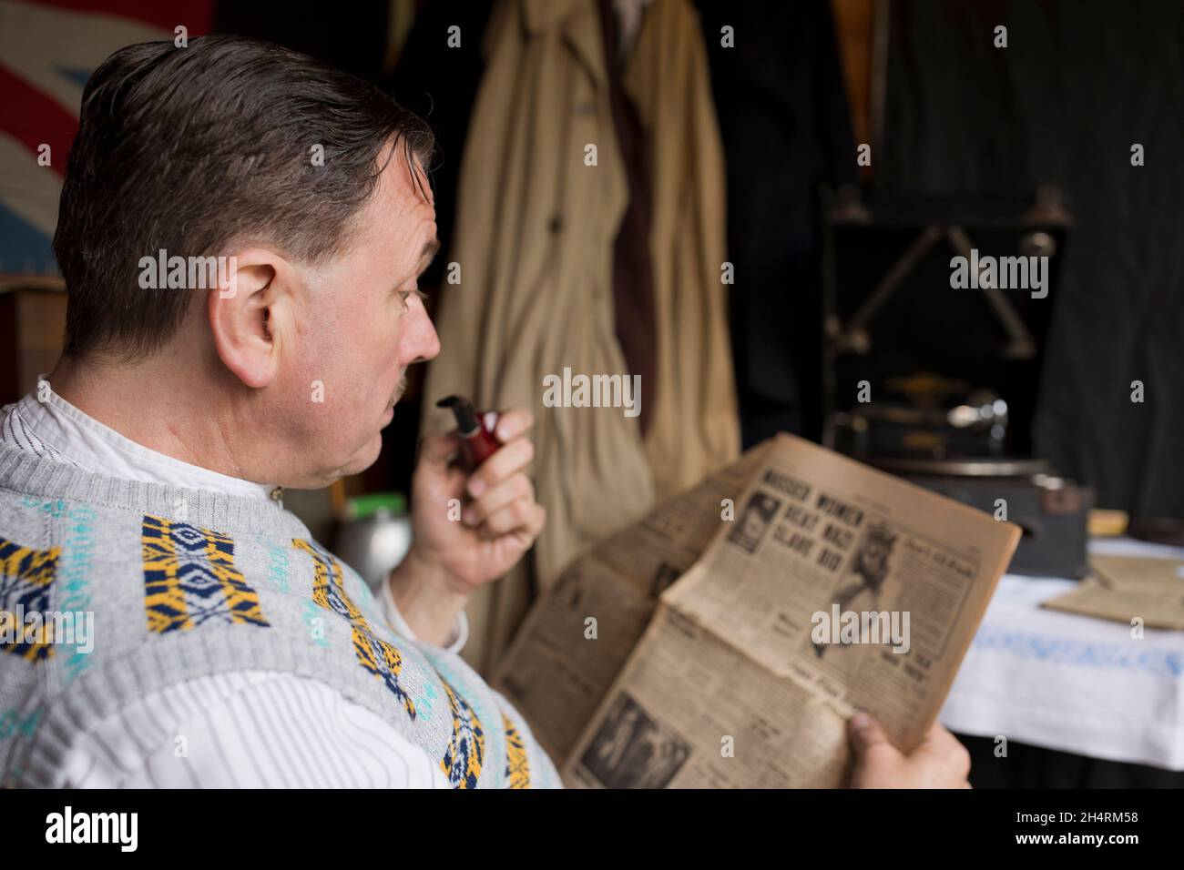 Royaume-Uni des années 1940 : l'homme fume la pipe, lisant le journal tout en listentant au disque gramophone. Banque D'Images