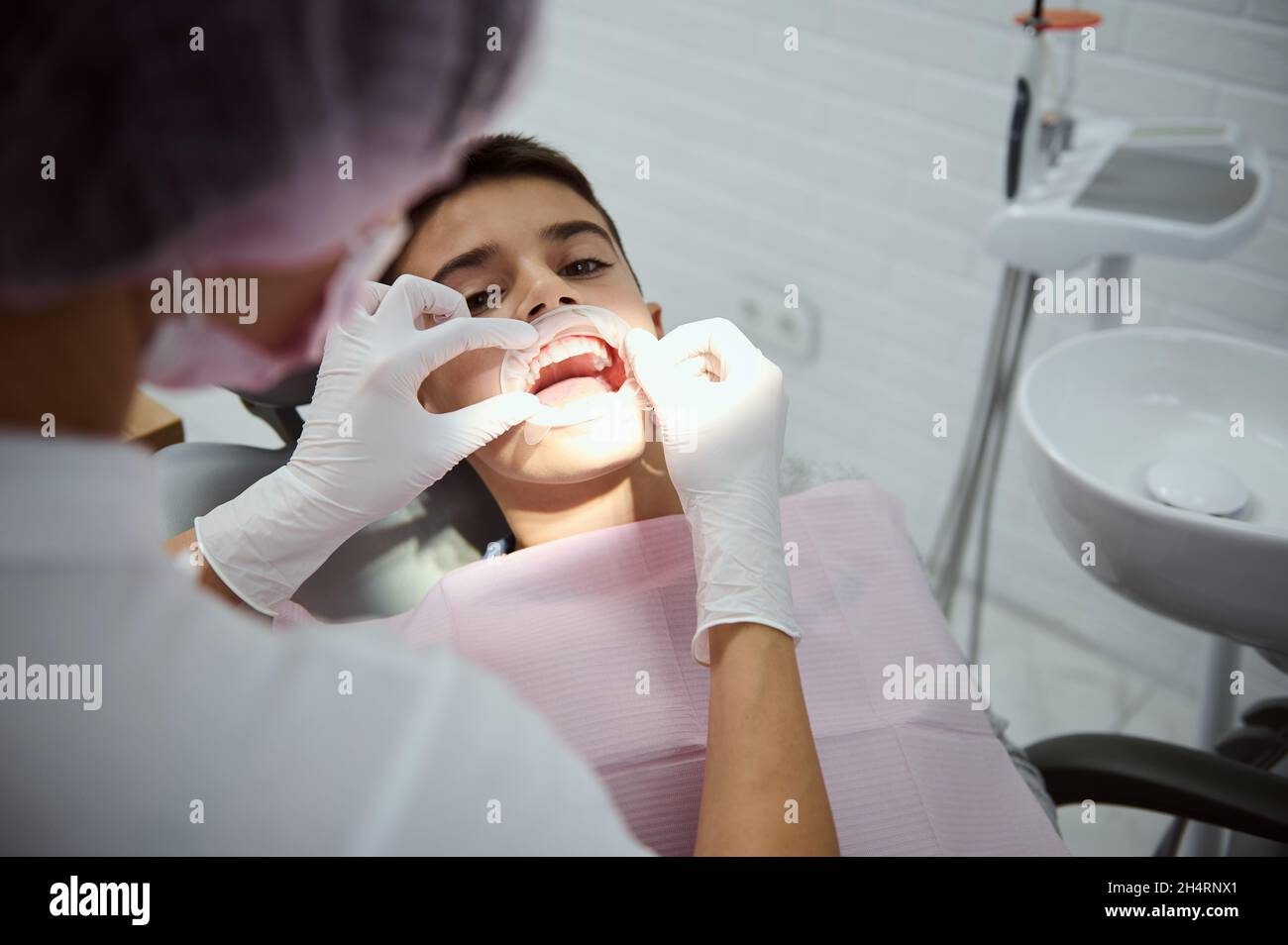 Vue de la tête d'un dentiste pédiatrique mettant un écarteur dentaire de joue sur un patient enfant avant un traitement oral.Garçon d'école au rendez-vous du dentiste.Coin détente Banque D'Images Vue de la tête d'un dentiste pédiatrique mettant un écarteur dentaire de joue sur un patient enfant avant un traitement oral.Garçon d'école au rendez-vous du dentiste.Coin détente Banque D'Images