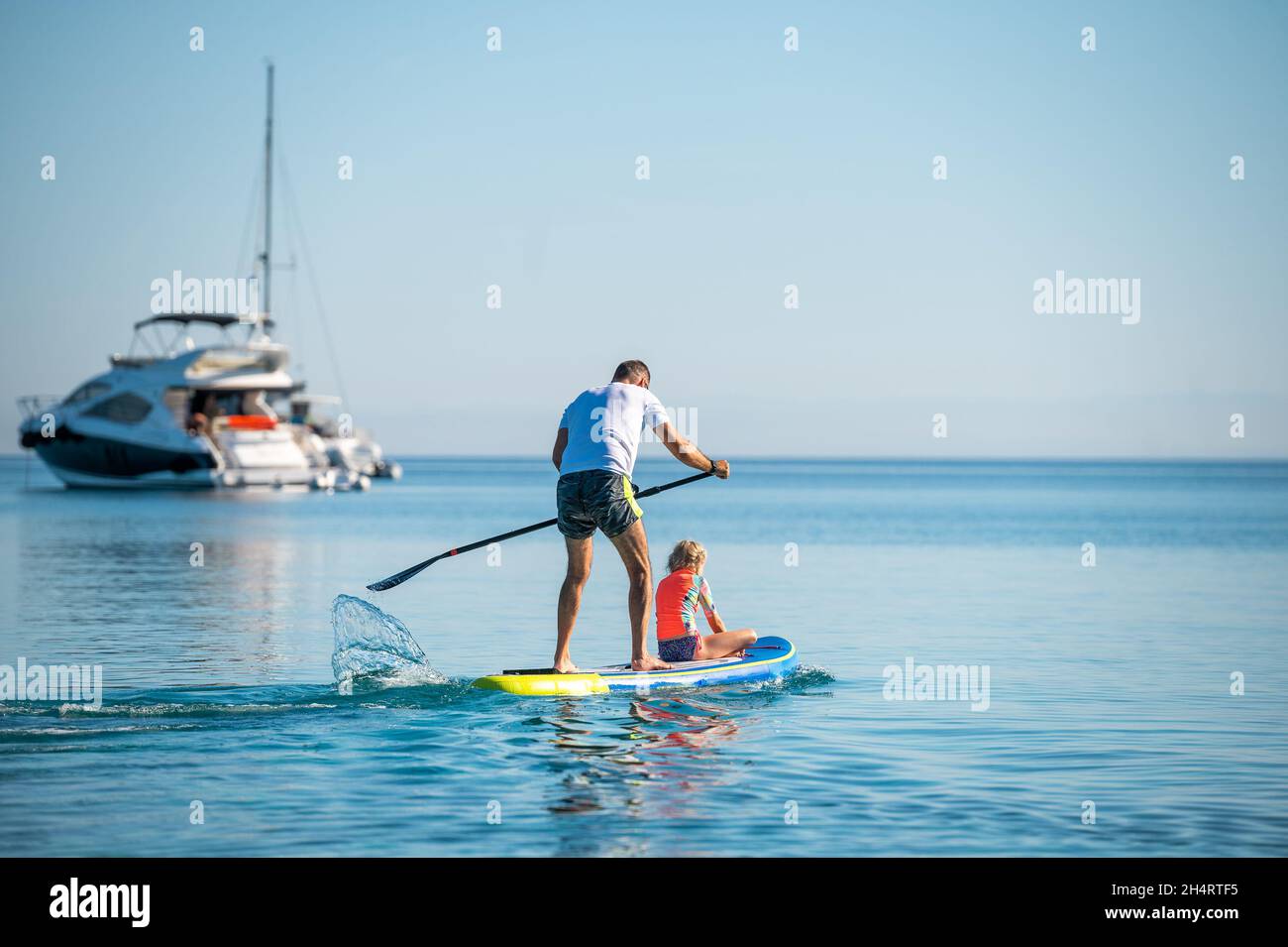 Le père et la fille à bord du SUP se tiennent debout pagayer pendant les vacances.Une famille active à cheval sur des planches SUP et à pagayer dans l'océan dans la belle soirée.Athlet Banque D'Images