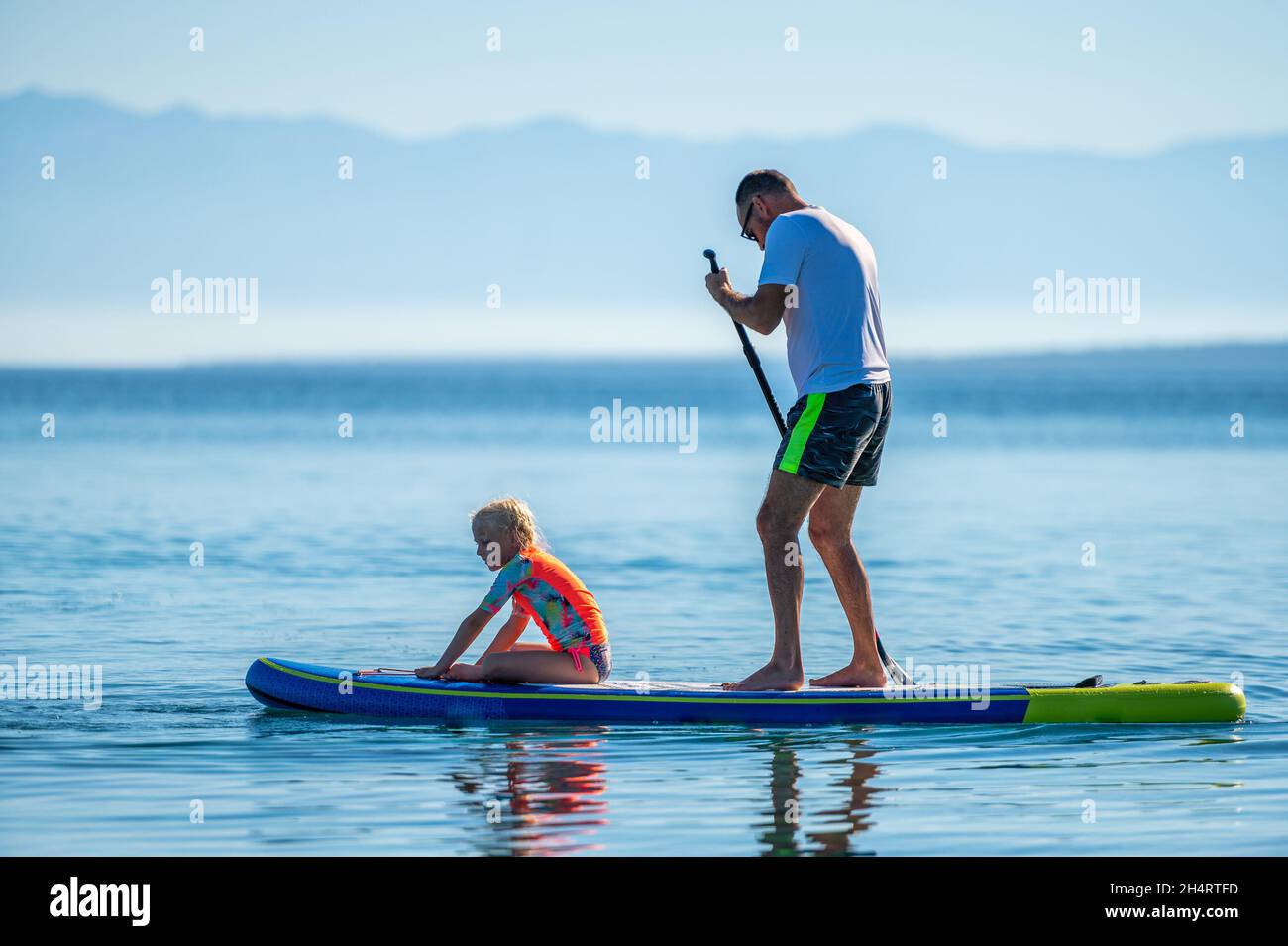 Le père et la fille à bord du SUP se tiennent debout pagayer pendant les vacances.Une famille active à cheval sur des planches SUP et à pagayer dans l'océan dans la belle soirée.Athlet Banque D'Images