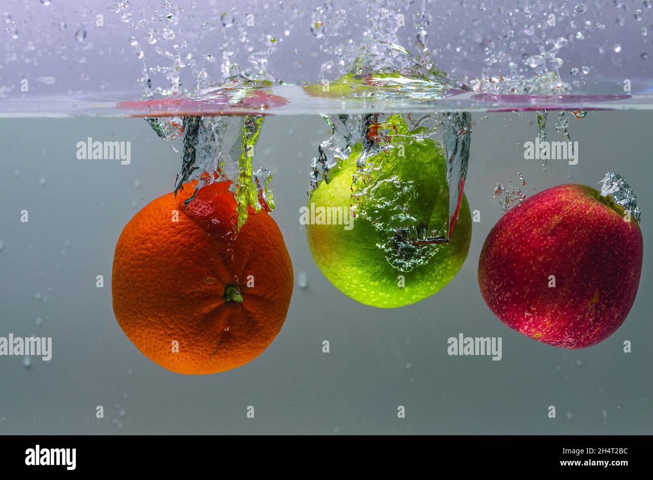 Vue rapprochée des pommes colorées et de l'orange tombant dans l'eau en arrière-plan. Banque D'Images