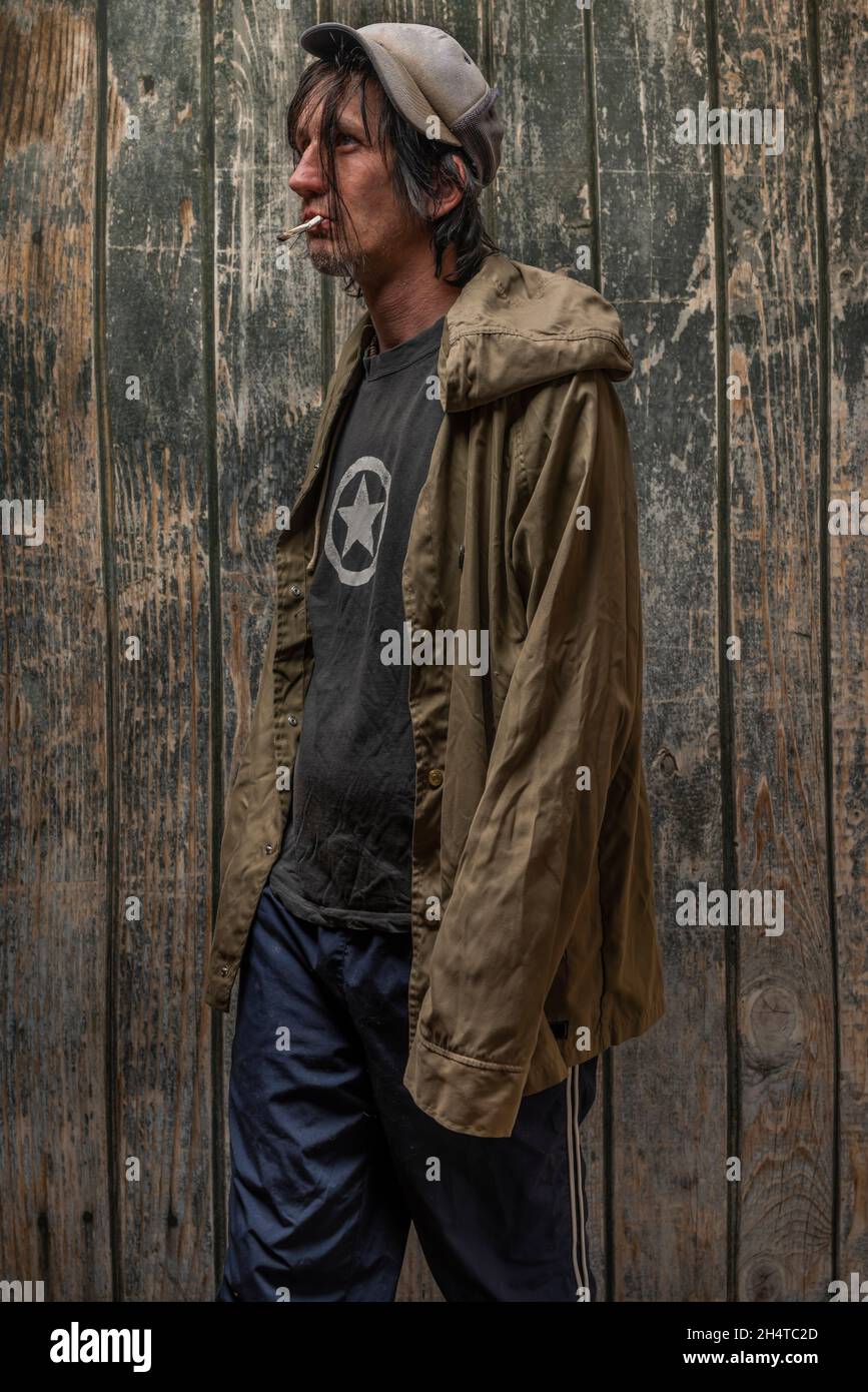 Junkie homme avec chapeau vert anorak et bleu pantalon de sueur près de vieux mur en bois Banque D'Images