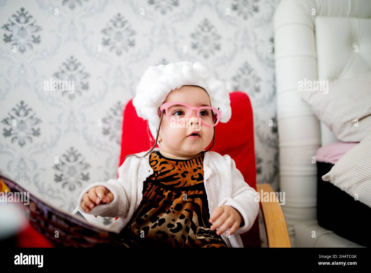 Bébé fille joueur assis dans une chaise.Porter un costume de granny avec des lunettes. Banque D'Images