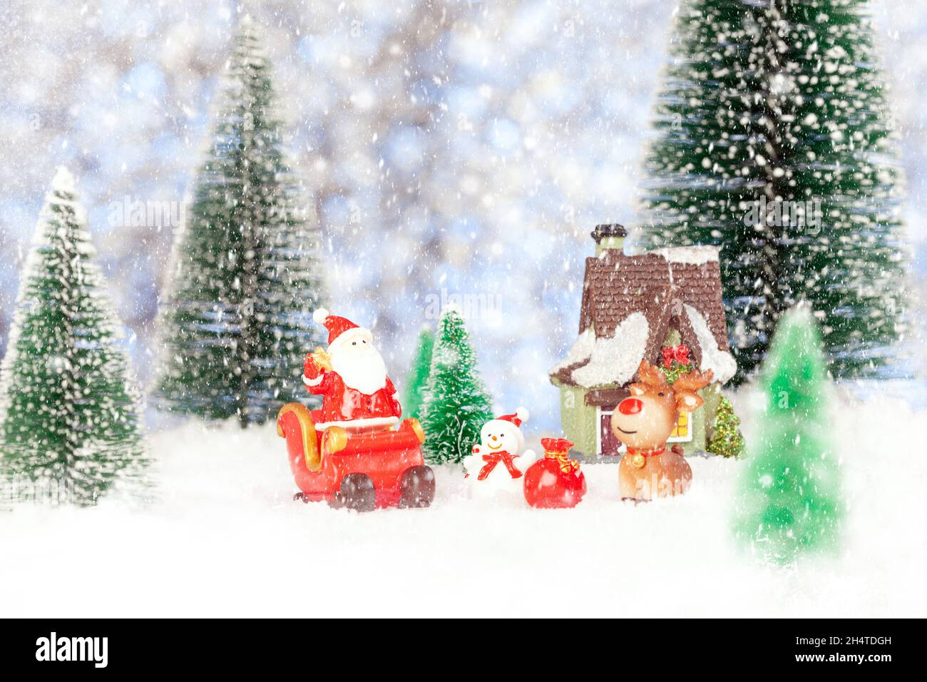 Carte postale de vœux du nouvel an.Un Père noël jouet se tient sur un traîneau de Noël.À proximité, il y a une maison de jouets, un bonhomme de neige, un cerf.Neige.Autour de sapin jouet Banque D'Images