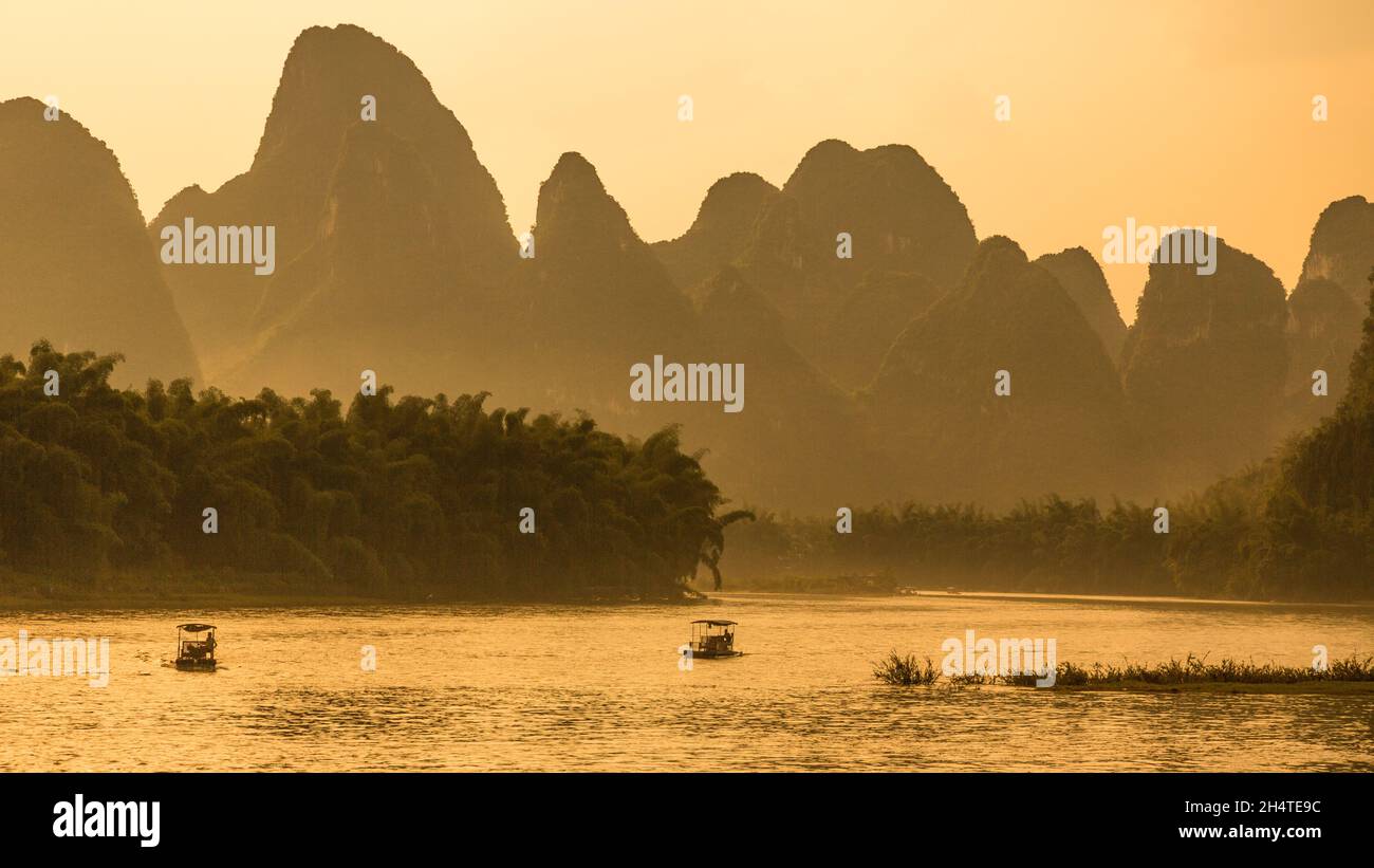 De petits radeaux motorisés retournent à Xinsping sur la rivière Li au coucher du soleil avec des collines de karst calcaire derrière.Chine. Banque D'Images