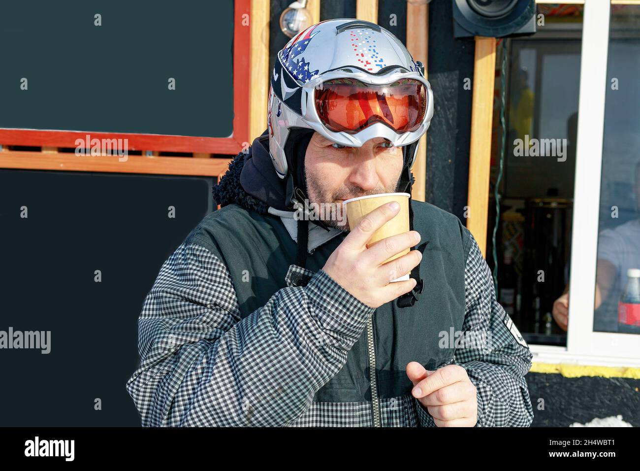 Portrait d'un snowboardeur avec une tasse de papier de café chaud.Homme d'origine caucasienne d'âge moyen dans un casque de sécurité reposant sur une pente de ski et buvant Banque D'Images