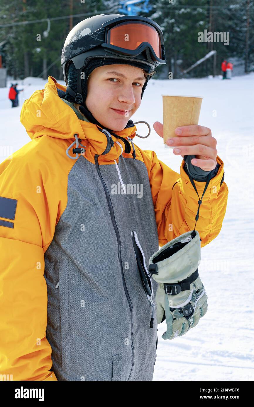 Le snowboardeur boit du café chaud.Un jeune homme d'origine caucasienne tient une tasse de papier avec une boisson chaude.Arrière-plan des pistes de ski.Portrait d'un AT Banque D'Images