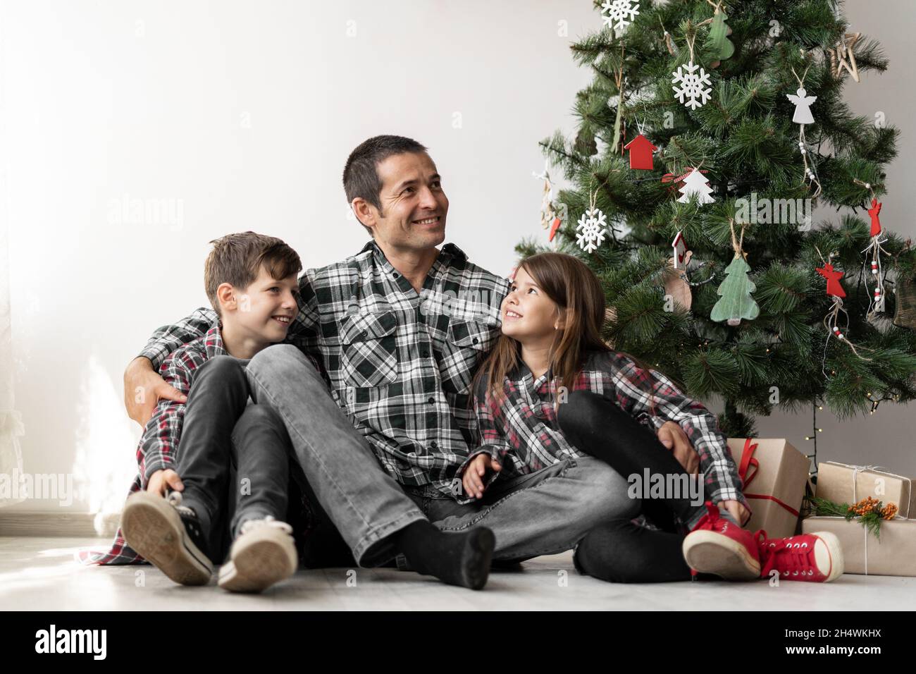 Gros plan d'une famille heureuse sous un arbre pour Noël ou le nouvel an.Papa avec son fils et sa fille à l'étage x-mas le matin. Banque D'Images