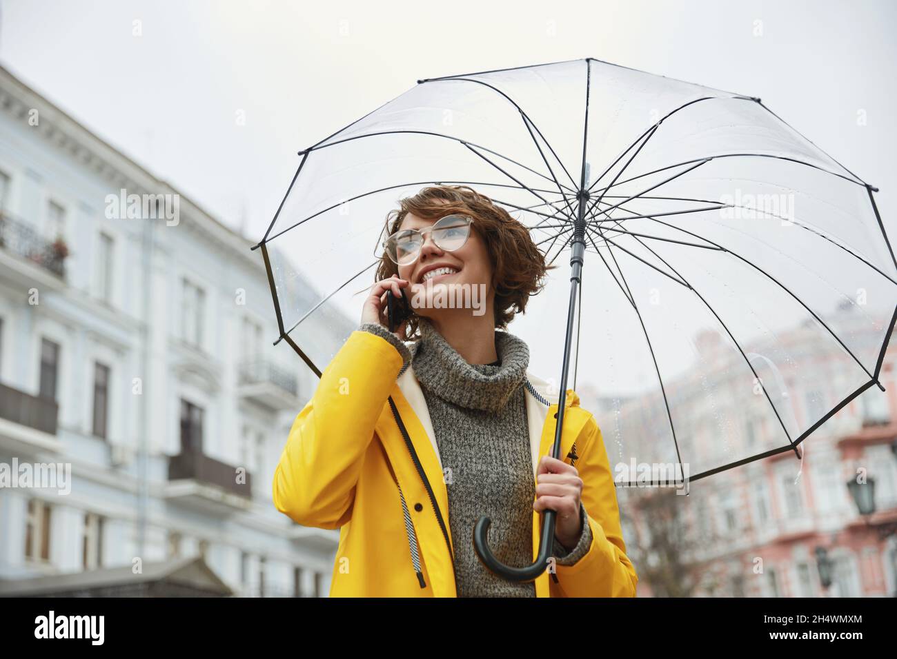 Fille caucasienne en imperméable jaune avec parapluie transparent en  ville.Jeune belle femme vêtue de vêtements de pluie tout en marchant dans la  rue le jour.Con Photo Stock - Alamy