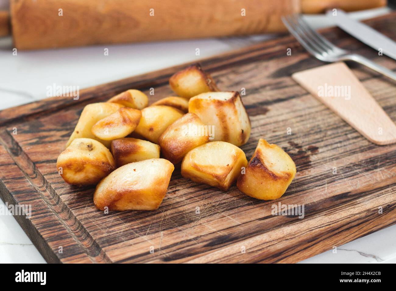 Pommes de terre rôties sur une planche à découper en bois sur un plan de travail de cuisine Banque D'Images