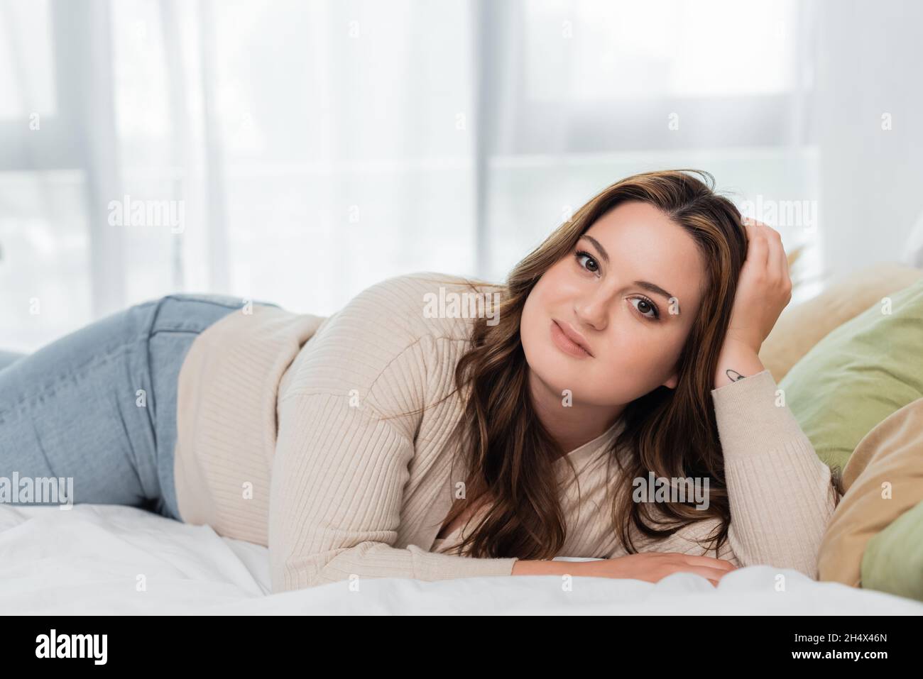 Jeune femme positive de corps regardant la caméra sur le lit Banque D'Images