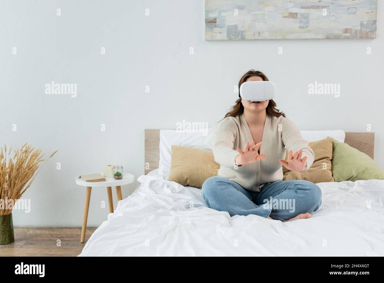 Brunette plus une femme de taille jouant dans un casque de réalité virtuelle sur le lit Banque D'Images