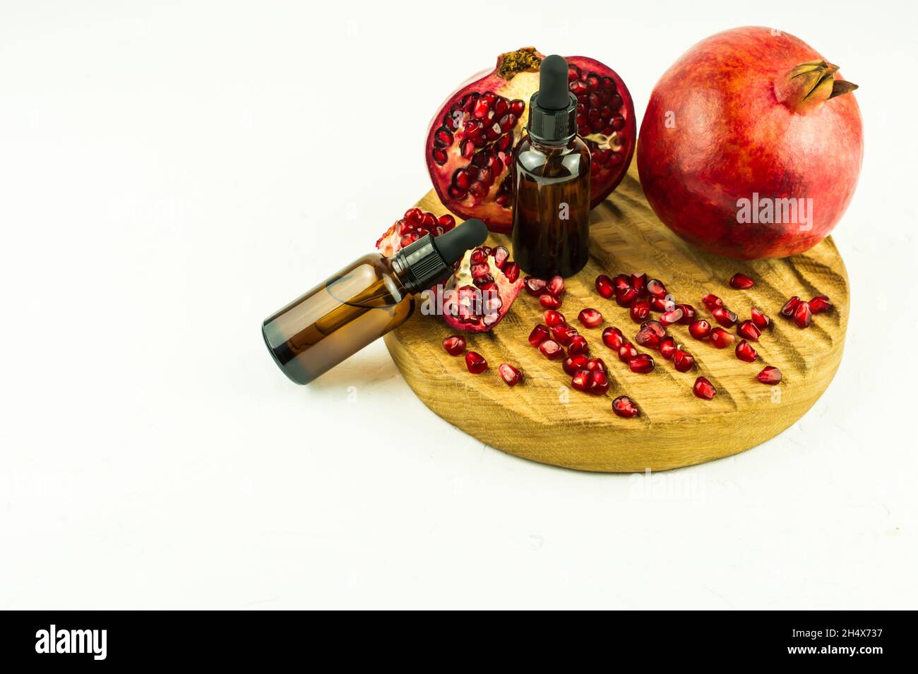 huile de grenade cosmétique ou huile essentielle en bouteilles de gouttes pour les soins naturels de la peau sur un panneau rond en bois et un fond blanc Banque D'Images