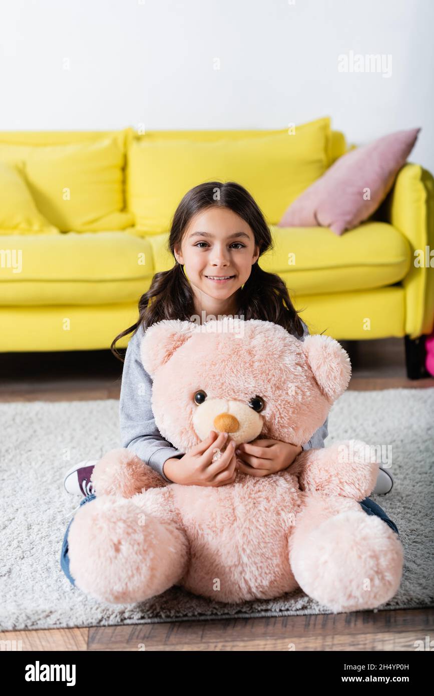 une jeune fille joyeuse tenant un jouet doux tout en étant assise sur un tapis à la maison Banque D'Images