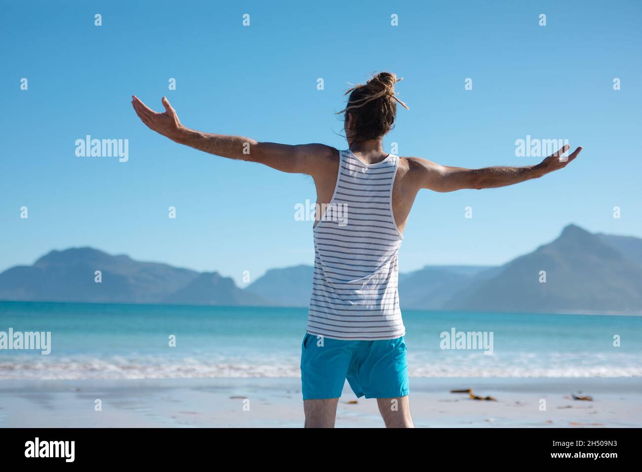 Vue arrière d'un homme debout avec les bras étirés tout en regardant vers la mer contre le ciel bleu Banque D'Images