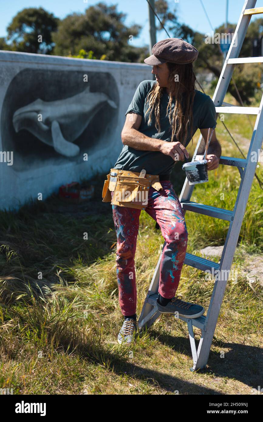 Un artiste masculin s'est penché sur l'échelle tout en regardant en arrière la peinture murale des baleines sur le mur Banque D'Images