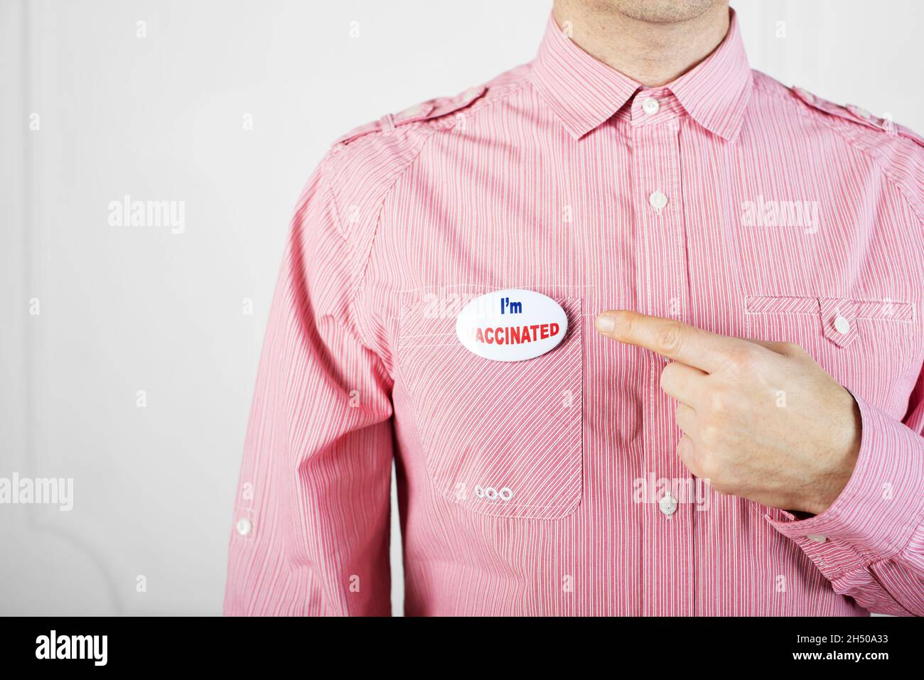 Homme de race blanche d'âge moyen en chemise rouge pointant avec son doigt sur la goupille de bouton avec le texte je suis vacciné Banque D'Images