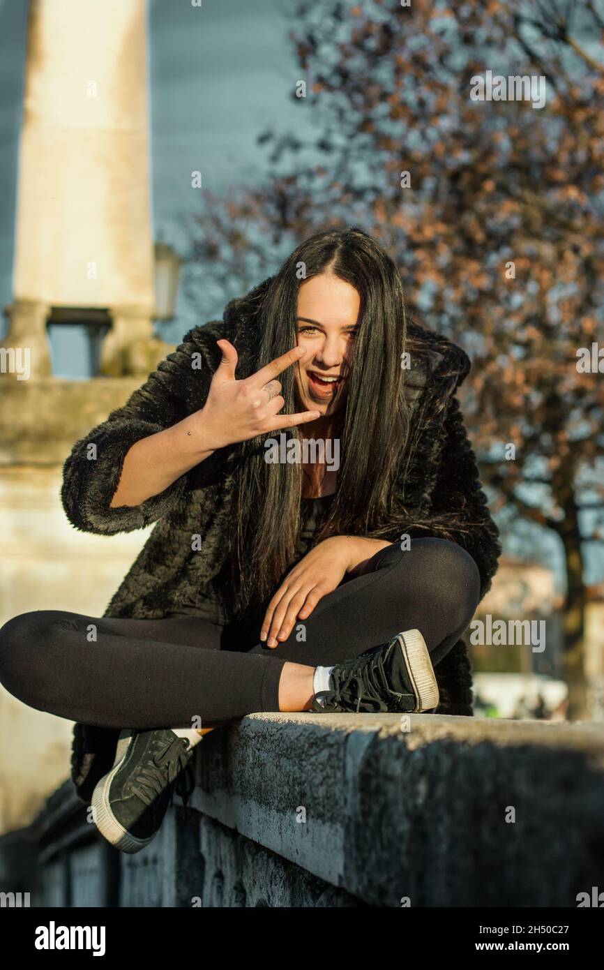 Funky adolescente fille de gang de rue fait cool gestes morsures lèvre  inférieure a des tresses porter des lunettes de soleil orange la veste  noire tendance a du plaisir au public pla