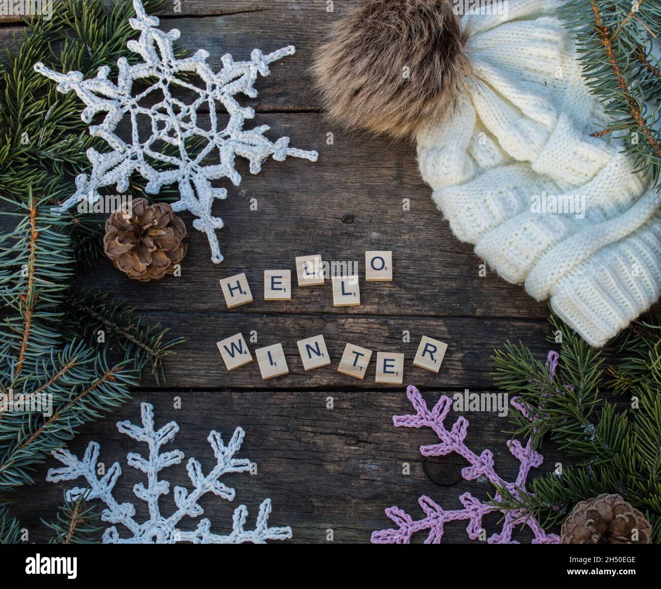 décorations en forme de flocon de neige en crochet sur sol en bois avec textes d'hiver et branches et cônes en sapin et fond de chapeau de galet tricoté Banque D'Images