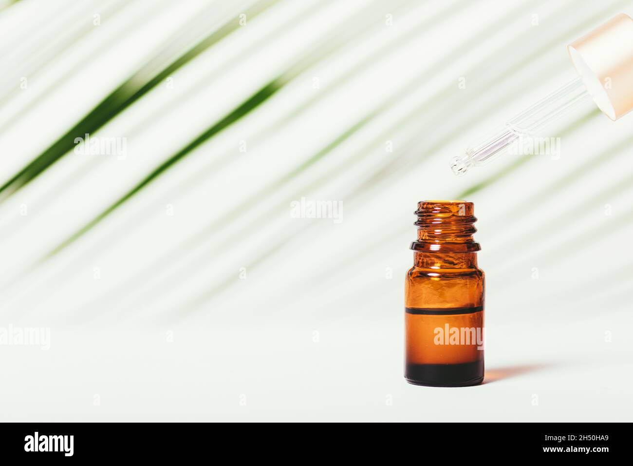 L'huile essentielle s'écoule de la pipette à la bouteille sur fond blanc avec une feuille verte.Copier l'espace Banque D'Images