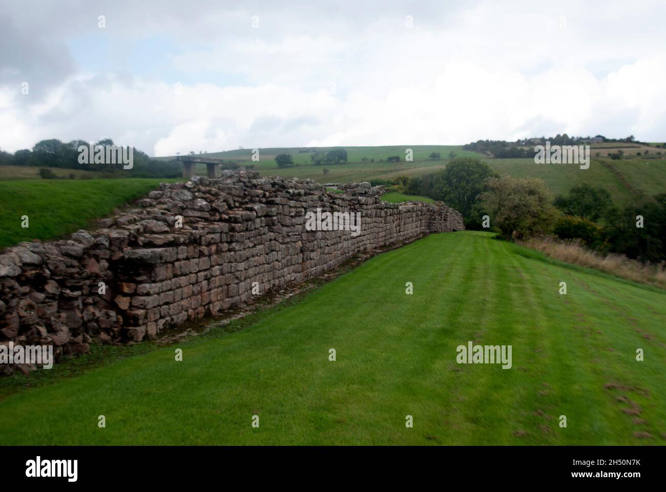 Mur de soutènement en pierre avec pelouses et arbres avec ciel nuageux au fort de Vindolanda et au musée, moulin de Bardon, Hexham, Northumberland, Angleterre,ROYAUME-UNI Banque D'Images