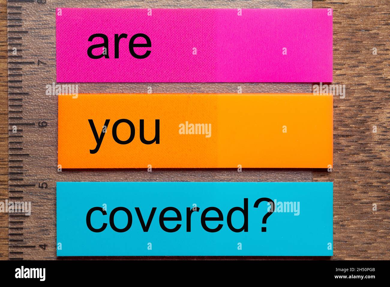 Trois autocollants de signet avec l'expression êtes-vous couvert ?sur une table en bois naturel foncé Banque D'Images