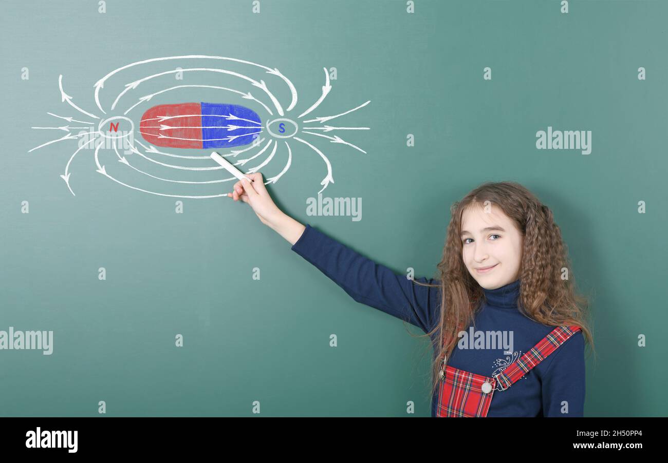 La pré-adolescente parle de champs magnétiques, expliquant le sujet à partir de photos en couleur avec de la craie sur un tableau noir.Photo haute résolution.Service complet Banque D'Images