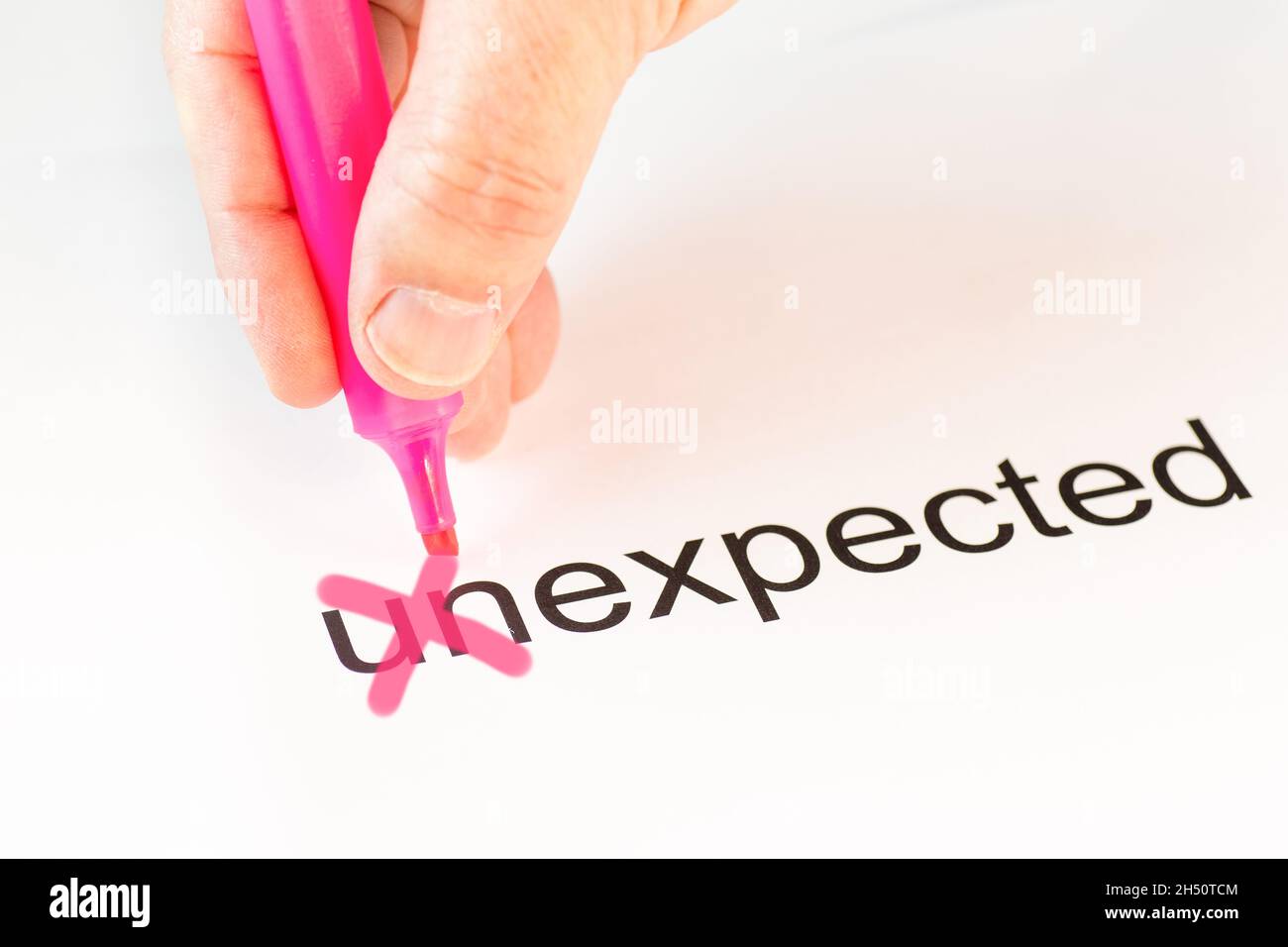 Le préfixe « un » du mot inattendu est barré d'une main avec un crayon rose Banque D'Images
