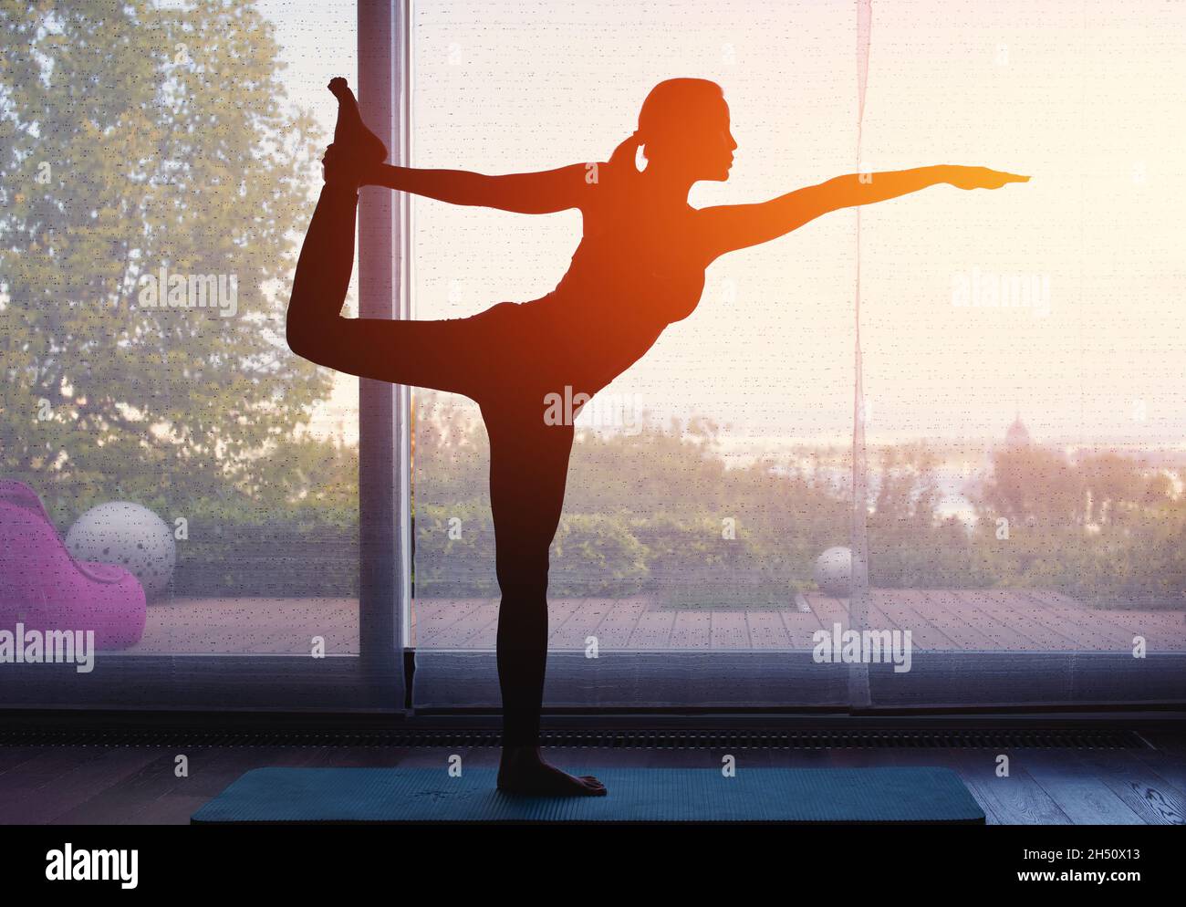 Silhouette de jeune femme faisant du yoga à la maison au coucher du soleil orange Banque D'Images