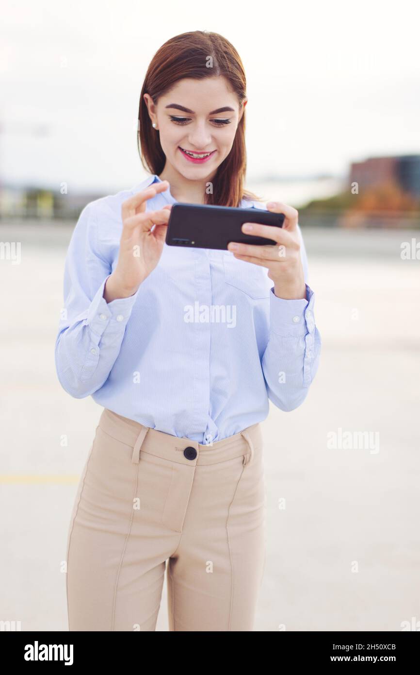 Jeune redhead caucasien smiley femme d'affaires messagerie sur smartphone à l'extérieur Banque D'Images
