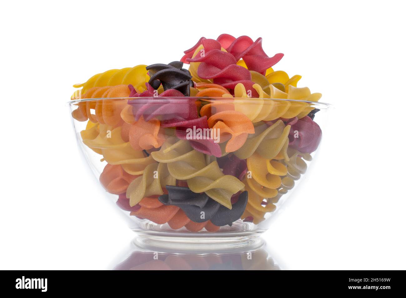 Pâtes fusilli colorées non cuites avec verrerie, gros plan, isolées sur du blanc. Banque D'Images