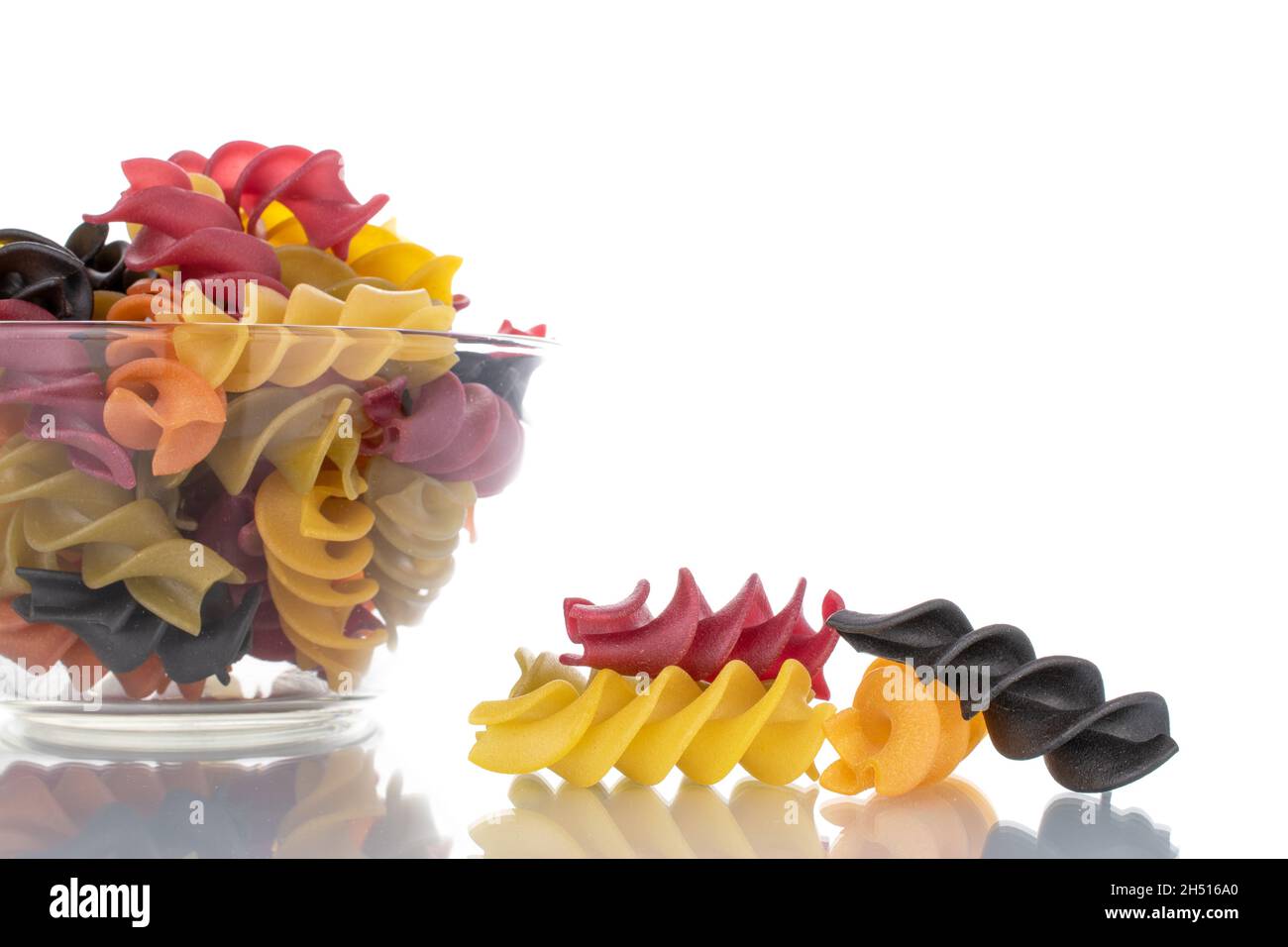 Pâtes fusilli colorées non cuites avec verrerie, gros plan, isolées sur du blanc. Banque D'Images