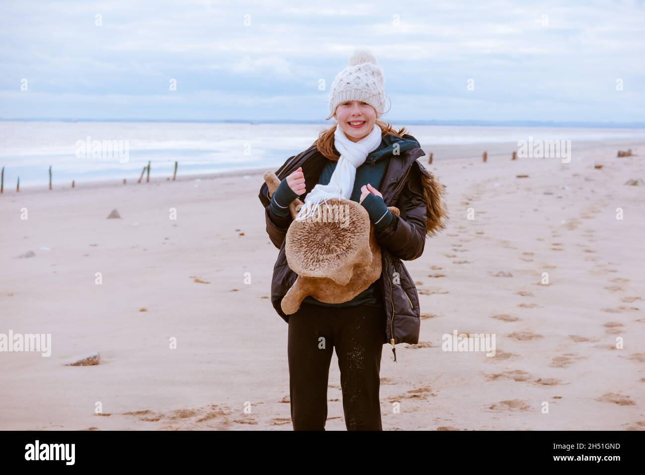 Une jeune adolescente sur une promenade à la plage explorant la nature et tenant une vertèbre de baleine Banque D'Images