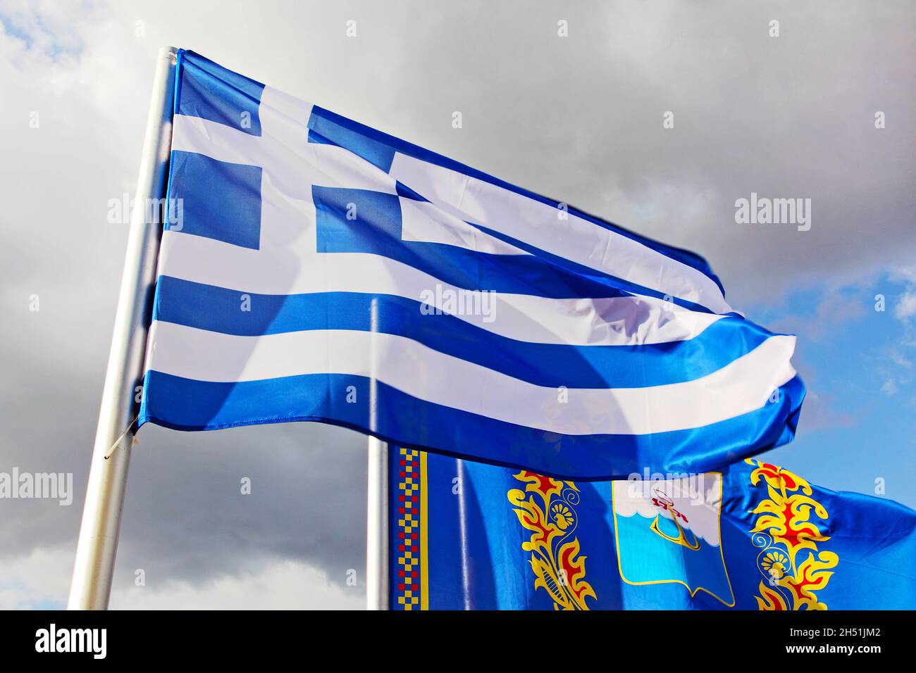 Drapeau grec et drapeau de la ville de Marioupol sur fond ciel nuageux lors du festival folklorique grec de Marioupol, en Ukraine. Banque D'Images