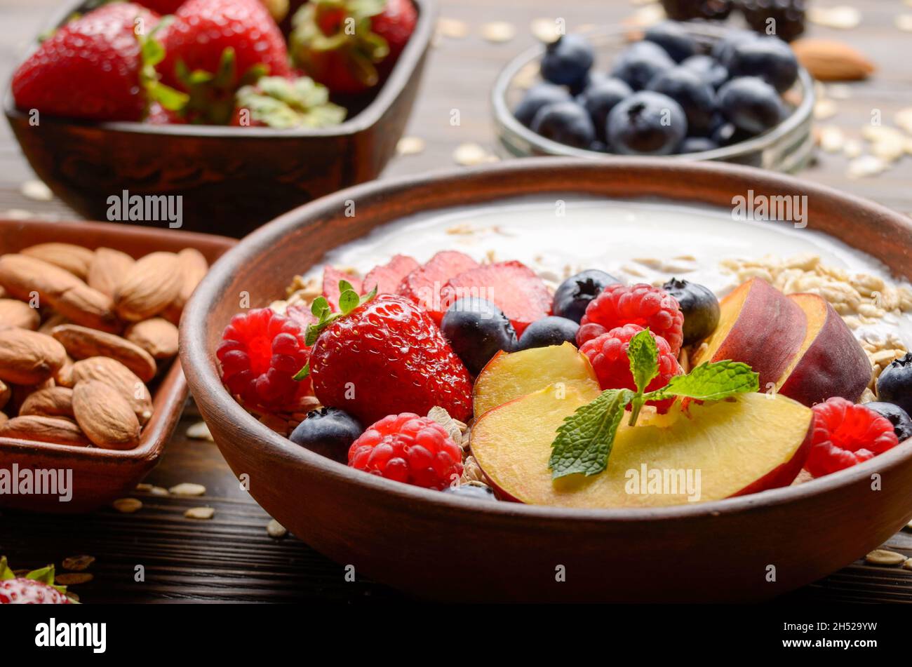 Muesli fruit sain avec des pêches amandes fraises et blackberry dans l'argile avec du yaourt sur table de cuisine en bois Banque D'Images