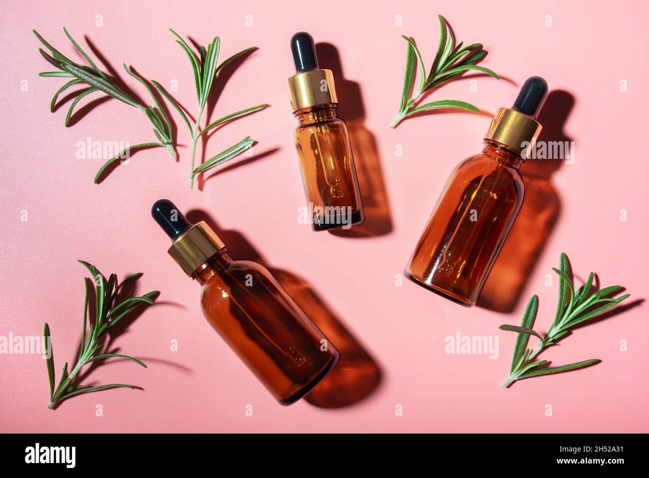 Flacons compte-gouttes avec feuilles d'huile et de romarin sur table rose, vue sur la pose.Concept de cosmétiques à base de plantes Banque D'Images